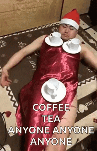 A Man In A Santa Hat Is Laying On The Floor With Cups Of Coffee On Plates Around His Waist . GIF