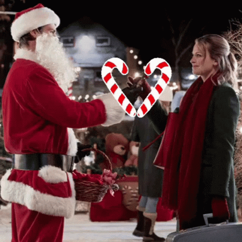 A Man In A Santa Suit Is Giving A Woman A Candy Cane In The Shape Of A Heart GIF