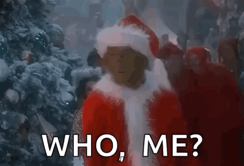 A Man In A Santa Suit Is Standing In Front Of A Christmas Tree And Asking Who Me . GIF