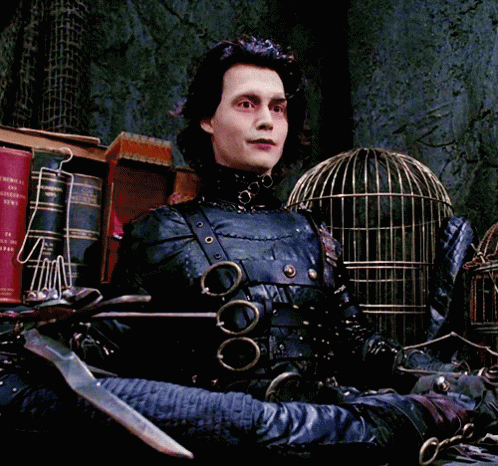 A Man In A Scissors Costume Is Sitting In Front Of A Cage GIF