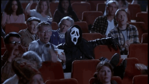 A Man In A Scream Mask Is Sitting In A Theater With Other People GIF