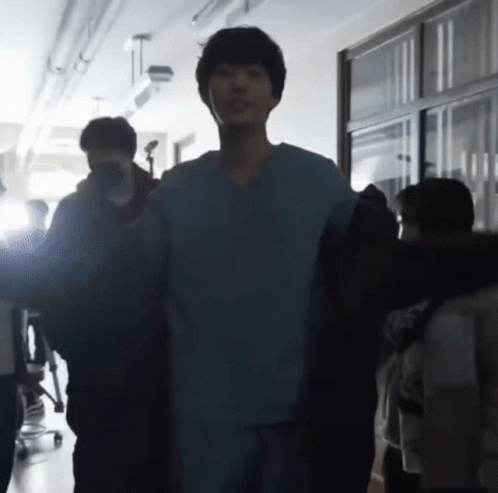 A Man In A Scrub Top Is Standing In A Hallway With A Group Of People GIF