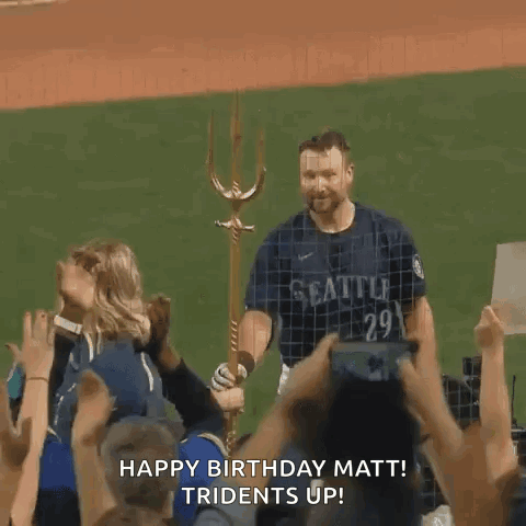 A Man In A Seattle Jersey Is Standing On A Baseball Field With A Trident In His Hand . GIF