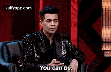 A Man In A Sequined Jacket Is Sitting In A Chair Holding A Cell Phone And Saying `` You Can Be . '' GIF