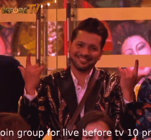 A Man In A Sequined Jacket Is Smiling And Making A Devil Horns Sign GIF