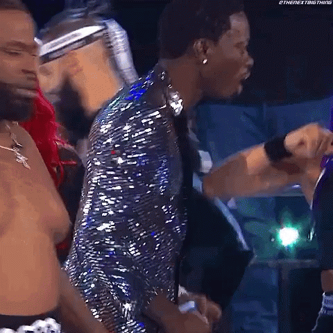 A Man In A Sequined Jacket Is Standing In Front Of A Group Of People . GIF