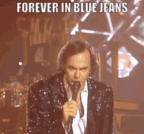 A Man In A Sequined Suit Is Singing Into A Microphone On Stage . GIF