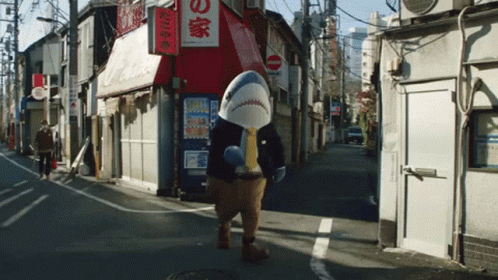 a man in a shark costume walks down a street in front of a store with chinese writing on it