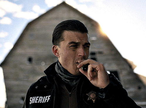 a man in a sheriff 's jacket talks on a walkie talkie