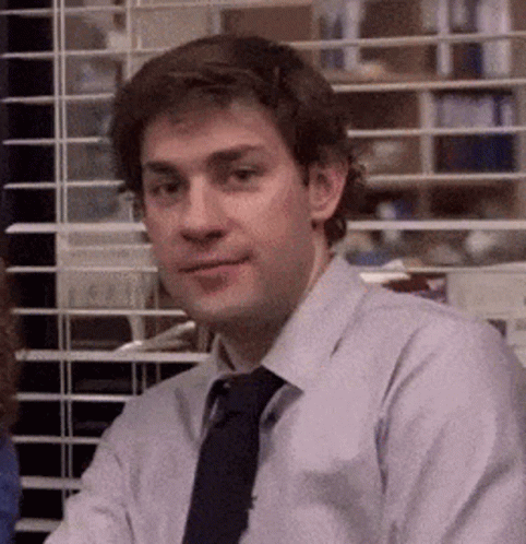 A Man In A Shirt And Tie Is Sitting In Front Of A Window In An Office . GIF