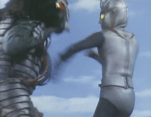 A Man In A Silver Suit Kicks Another Man In A Black Suit GIF