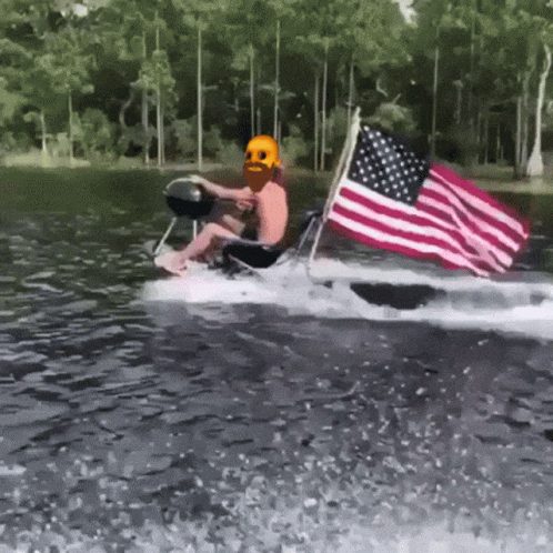 A Man In A Skull Mask Is Riding A Boat With An American Flag GIF