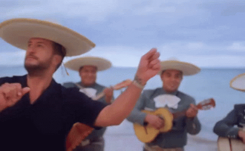 A Man In A Sombrero Is Dancing In Front Of A Band Of Mariachi Players GIF