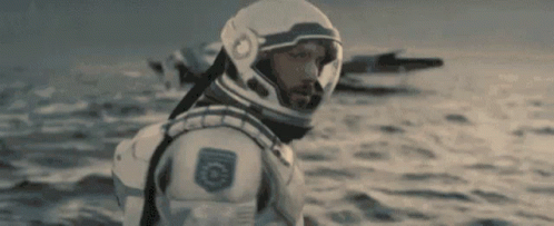A Man In A Space Suit And Helmet Is Standing In The Ocean . GIF
