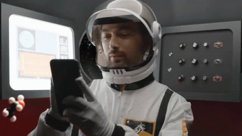 A Man In A Space Suit Is Looking At His Cell Phone GIF