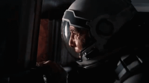 A Man In A Space Suit Is Smoking A Cigarette In A Room . GIF