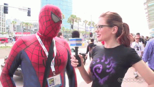 A Man In A Spider Man Costume Is Being Interviewed By A Woman GIF