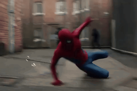 A Man In A Spiderman Costume Is Crawling On The Ground In Front Of A Brick Building . GIF