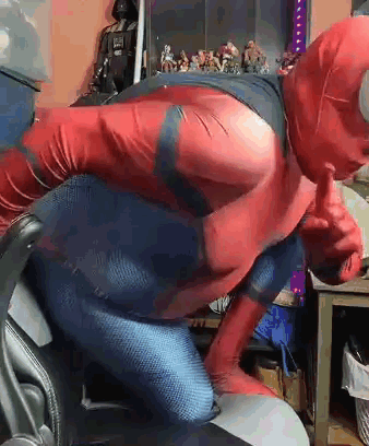 A Man In A Spiderman Costume Is Giving A Thumbs Up While Sitting In An Office Chair . GIF