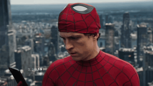 A Man In A Spiderman Costume Is Holding A Cell Phone In Front Of A City Skyline GIF