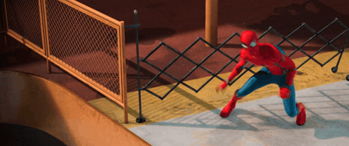 A Man In A Spiderman Costume Is Kneeling Down In Front Of A Chain Link Fence GIF