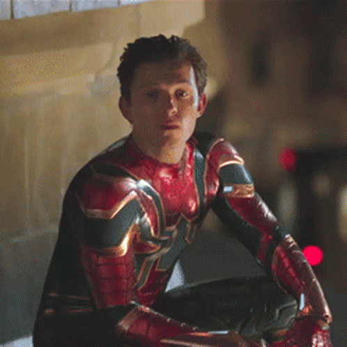 a man in a spiderman costume is sitting on a ledge looking at something .