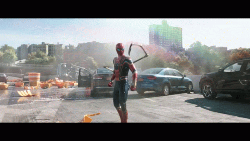 A Man In A Spiderman Costume Is Standing In A Parking Lot With Cars GIF