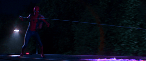 A Man In A Spiderman Costume Is Standing In Front Of A Street Light At Night GIF