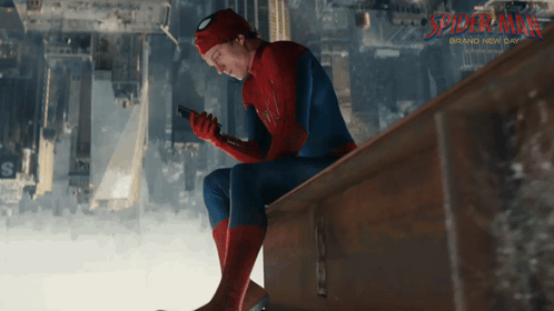 A Man In A Spiderman Costume Sits On A Railing Looking At His Phone GIF