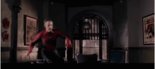A Man In A Spiderman Suit Is Jumping In The Air In A Room . GIF