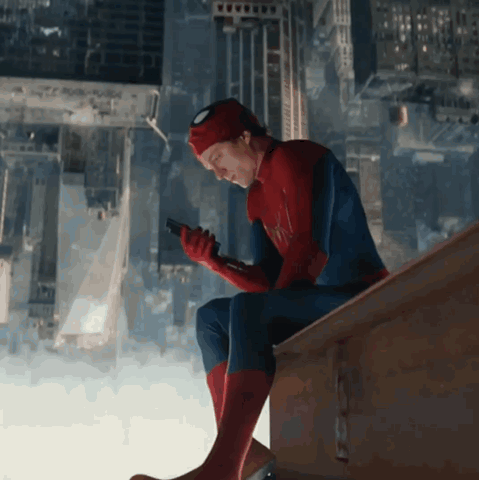 A Man In A Spiderman Suit Is Sitting On A Ledge Looking At His Phone GIF