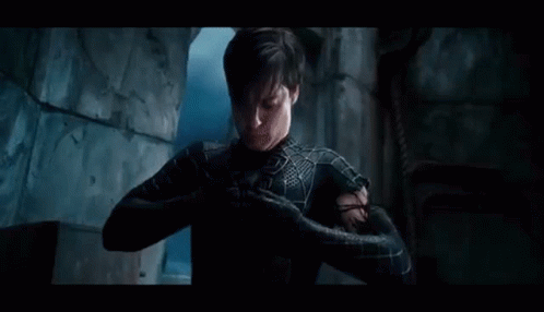 A Man In A Spiderman Suit Is Standing In A Dark Room With His Arms Outstretched . GIF