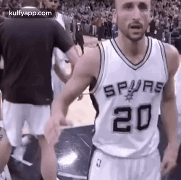 A Man In A Spurs Jersey Is Standing On A Basketball Court With His Hands In The Air . GIF