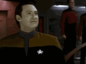 A Man In A Star Trek Uniform Is Making A Funny Face While Standing In Front Of A Group Of People . GIF