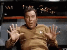 A Man In A Star Trek Uniform Is Sitting In A Chair With His Hands Up . GIF
