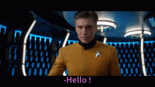 A Man In A Star Trek Uniform Says Hello In A Dark Room GIF