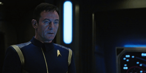 a man in a star trek uniform stands next to a sign that says hold on a second