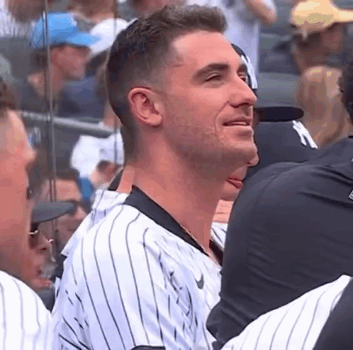 A Man In A Striped Baseball Uniform Is Sitting In A Stadium With Other People . GIF