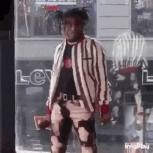 A Man In A Striped Jacket And Pants Is Standing In Front Of A Store . GIF