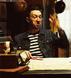 A Man In A Striped Shirt And Denim Jacket Is Sitting At A Desk GIF