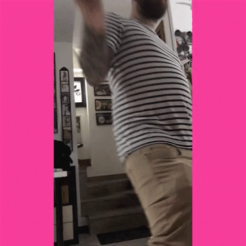 A Man In A Striped Shirt And Khaki Pants Is Standing In A Room GIF