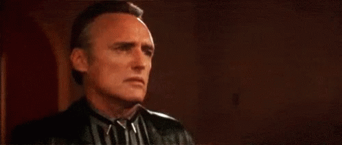 A Man In A Striped Shirt And Leather Jacket Is Looking At The Camera . GIF