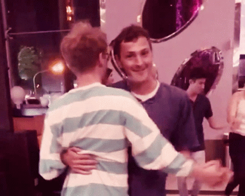 A Man In A Striped Shirt Hugs Another Man In A Blue Shirt GIF