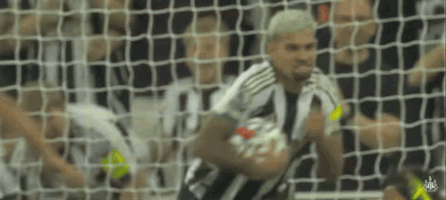 A Man In A Striped Shirt Is Holding A Soccer Ball In Front Of A Goal Net . GIF
