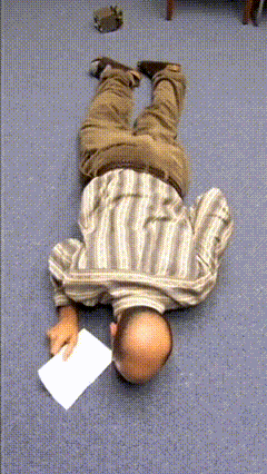 A Man In A Striped Shirt Is Laying On His Back On The Floor Holding A Piece Of Paper GIF