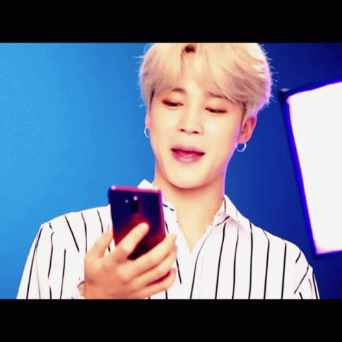 A Man In A Striped Shirt Is Looking At A Phone GIF