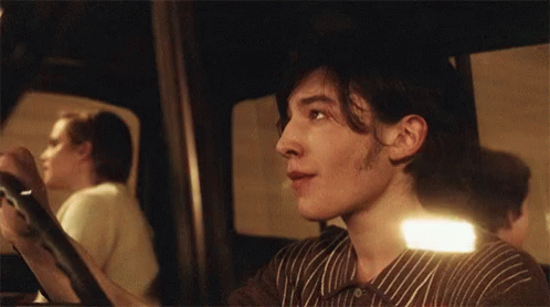 A Man In A Striped Shirt Is Looking At Something In A Mirror GIF