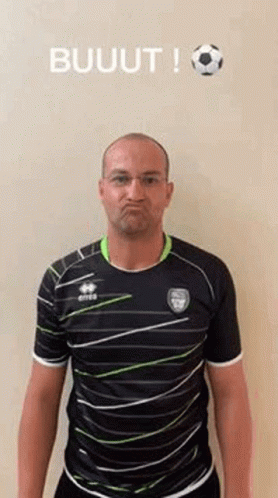 A Man In A Striped Shirt Is Making A Funny Face While Standing In Front Of A Soccer Ball . GIF
