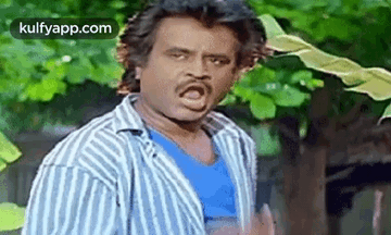 A Man In A Striped Shirt Is Making A Funny Face While Standing In Front Of A Tree . GIF