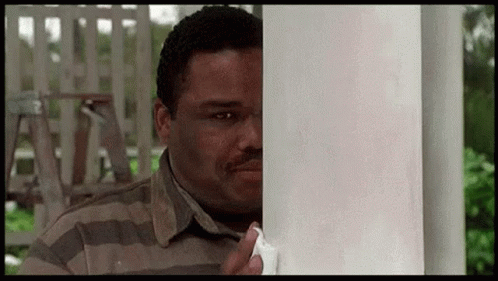 A Man In A Striped Shirt Is Peeking Around A Pole . GIF